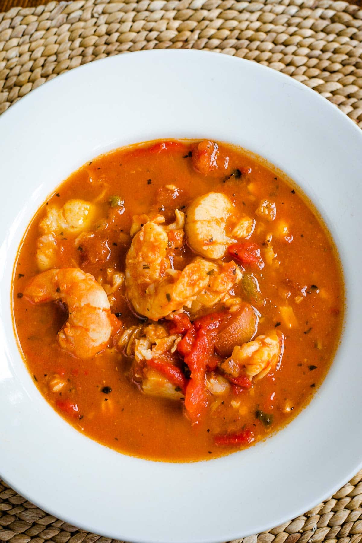 Shrimp and fish in tomato broth in white bowl.