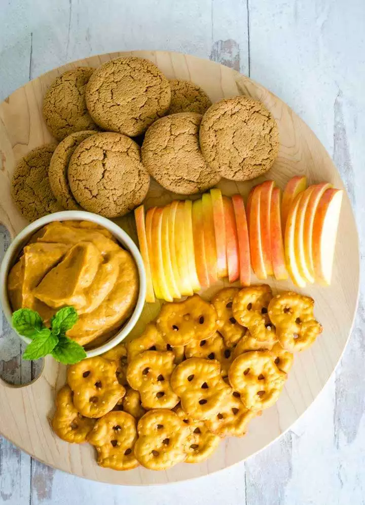 Ginger snaps, apple slices, pretzels, cream cheese dip on board