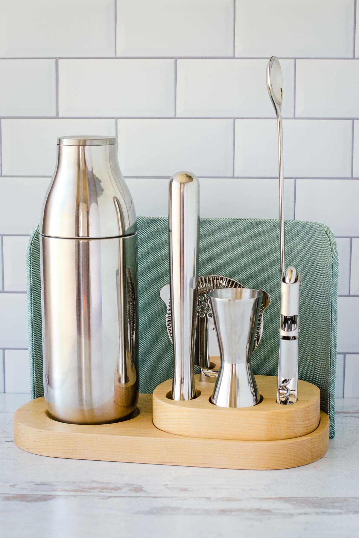 Bar set with shaker and bar tools on a light wood base with light blue back.