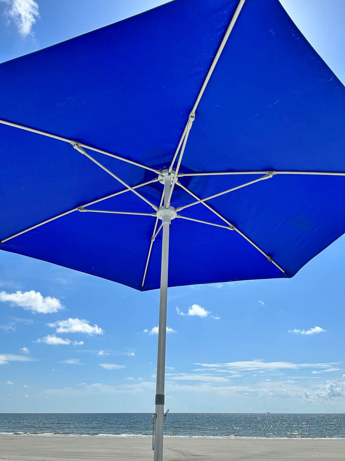 Blue umbrella with the sky, water and sand in the background.