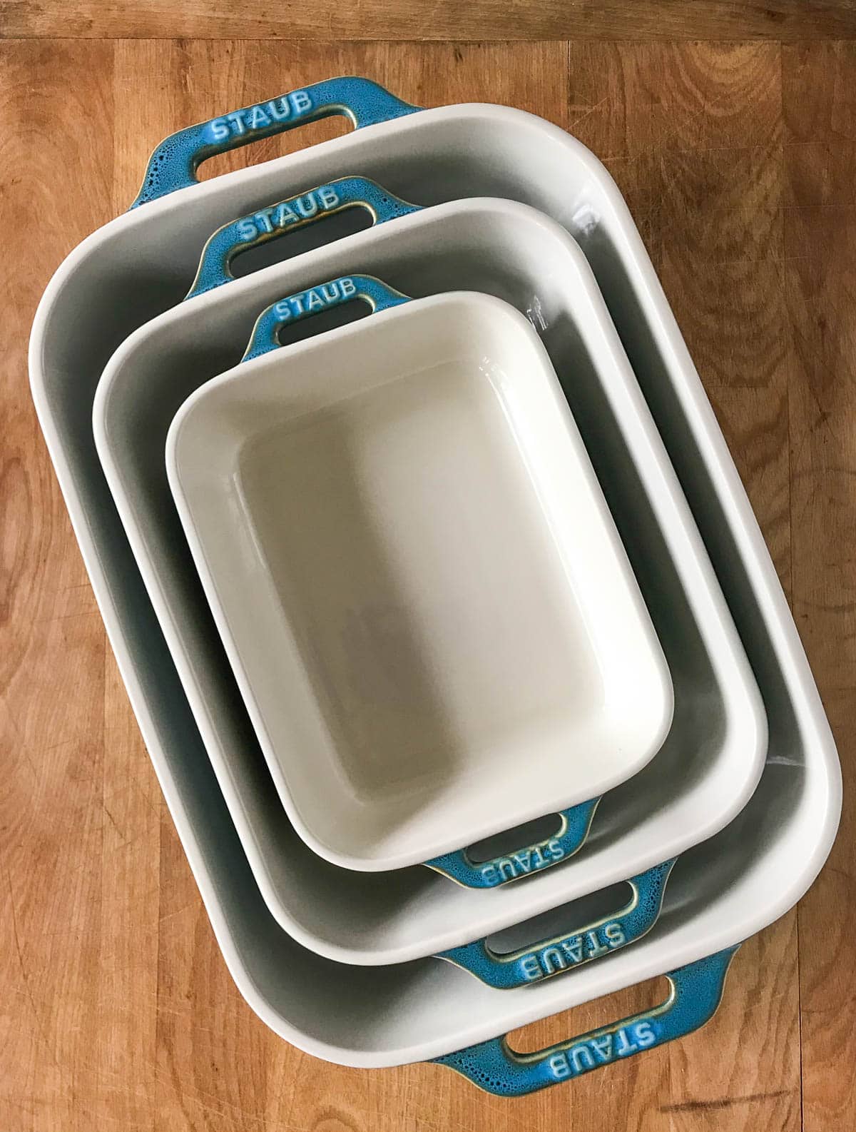 Three nesting blue and cream ceramic baking dishes on wood background.