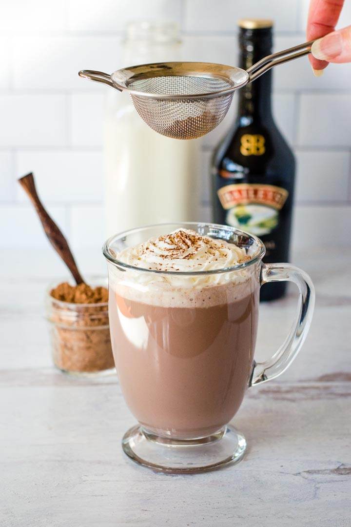 Sifting cocoa on whipped cream topping hot chocolate