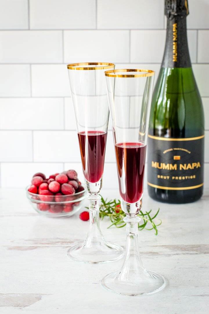 Pomegranate juice in flutes, champagne bottle, frozen cranberries, rosemary spring