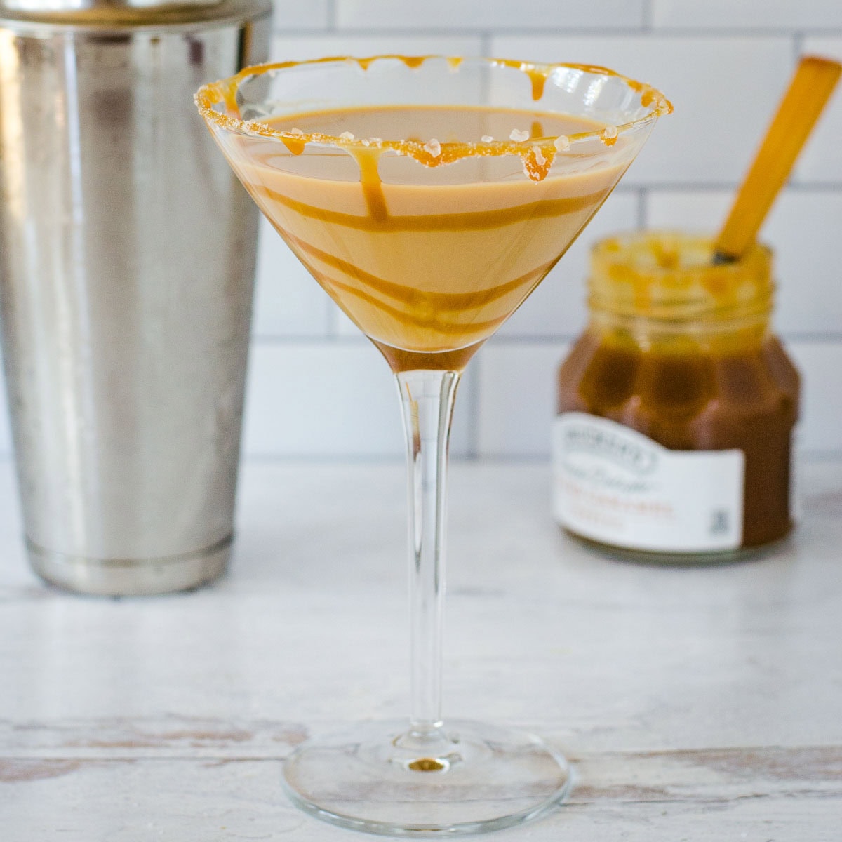 Salted caramel martini with cocktail shaker and jar of caramel sauce.