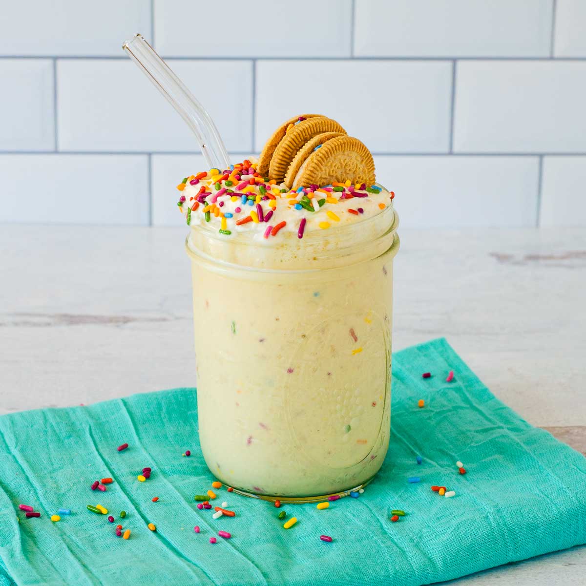 Birthday cake milkshake with rainbow sprinkles and cookies in mason jar with glass straw