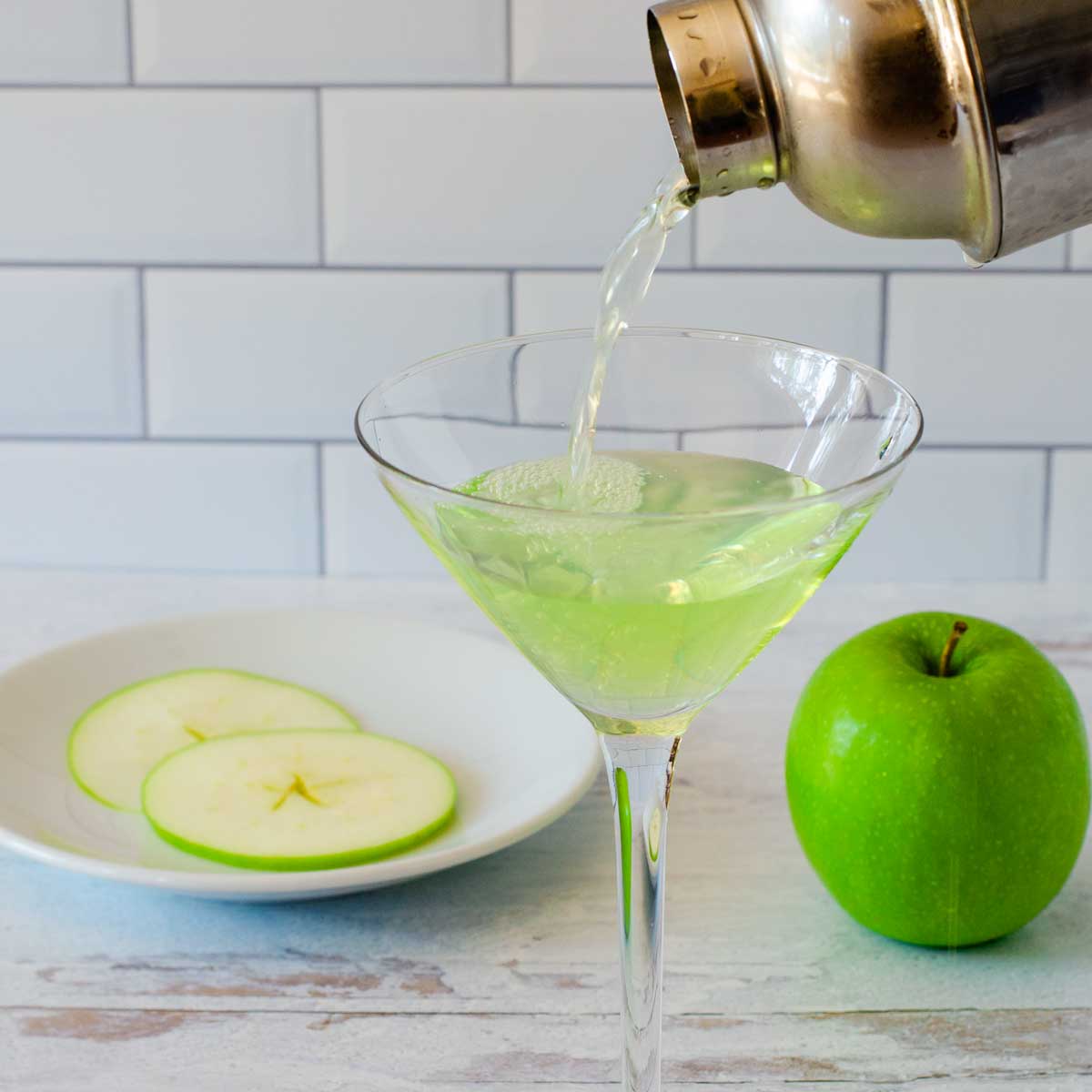 Appletini pouring into glass from cocktail shaker, green apple sliced