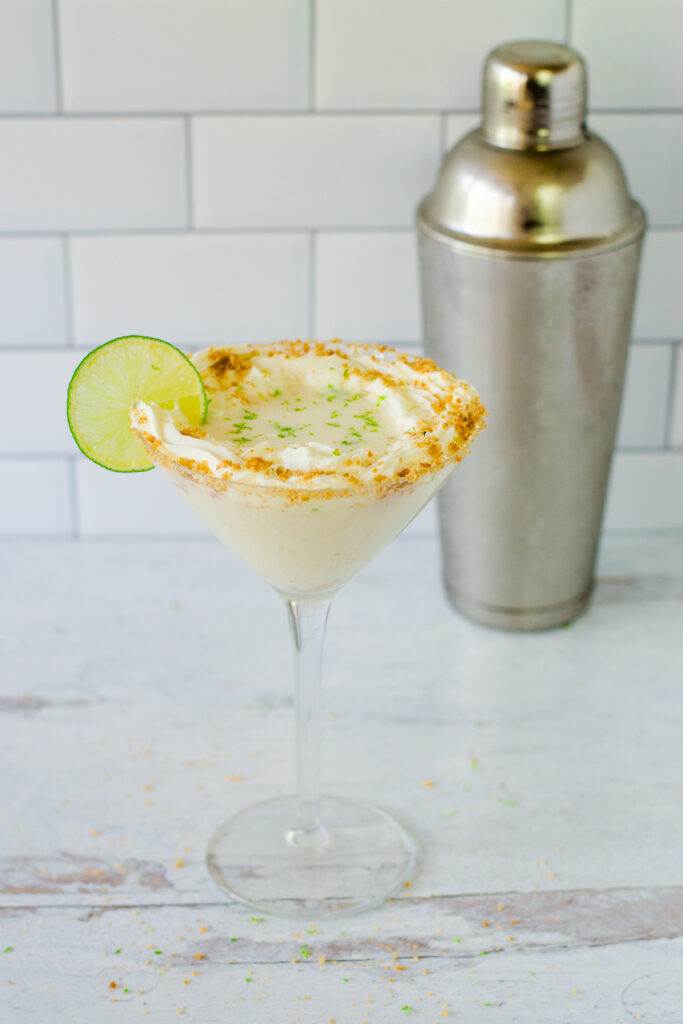 Key lime pie martini with whipped cream, graham cracker crumbs, lime zest and lime slice, cocktail shaker