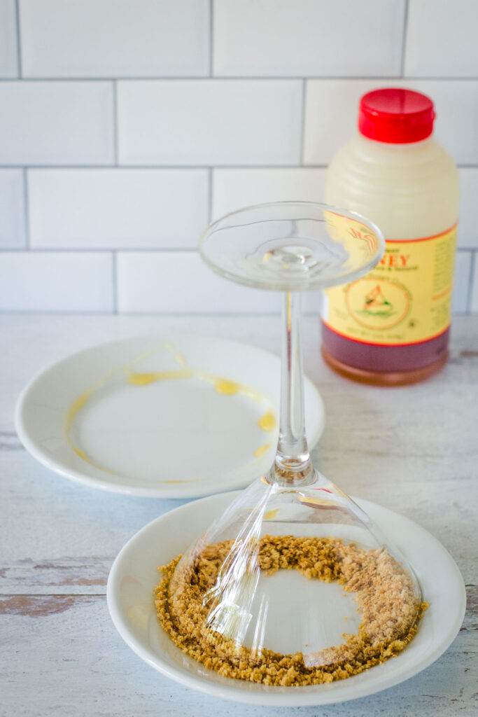 Small plate with honey, bottle of honey, small plate with martini glass dipping in cookie crumbs