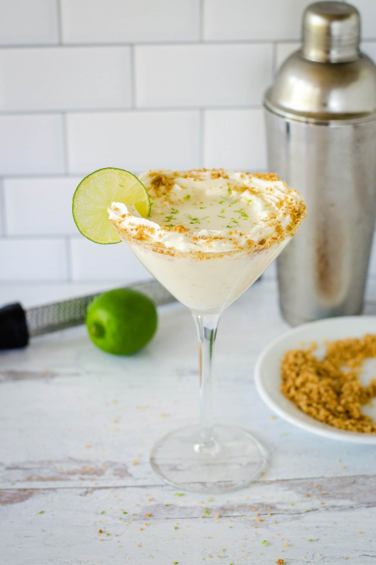Key lime pie martini with whipped cream, graham cracker crumbs, and lime slice, zester, lime, cocktail shaker