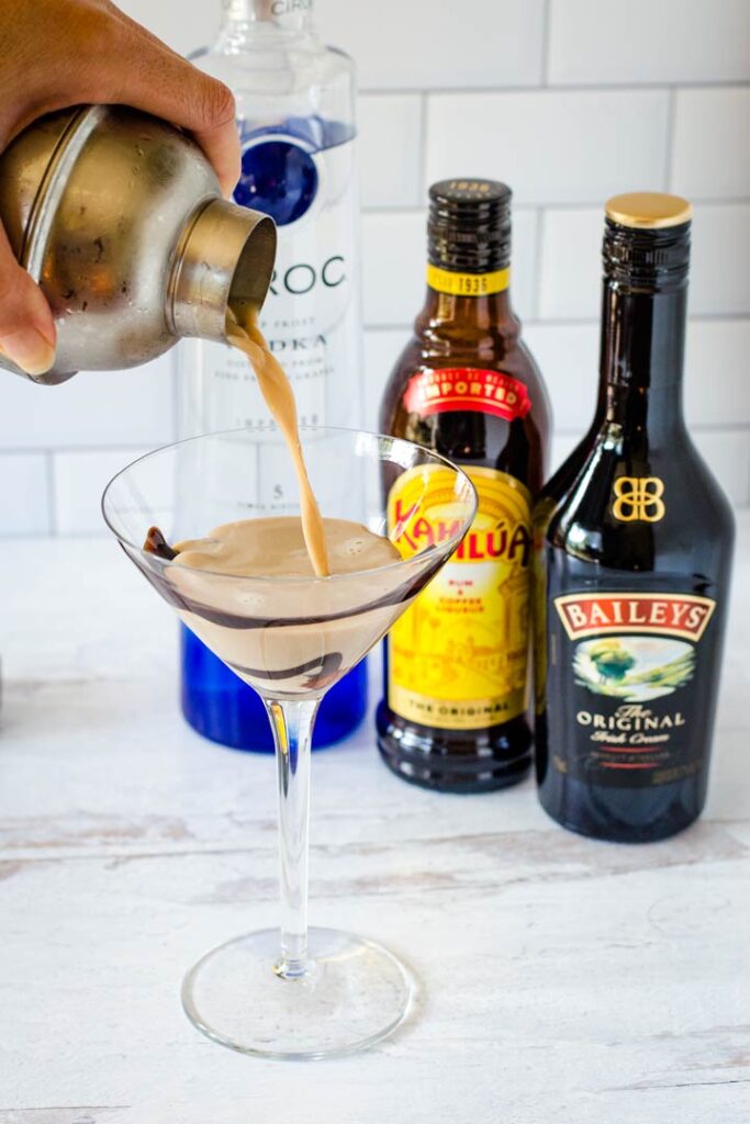 Pouring cocktail into martini glass next to vodka, Kahlua, Baileys