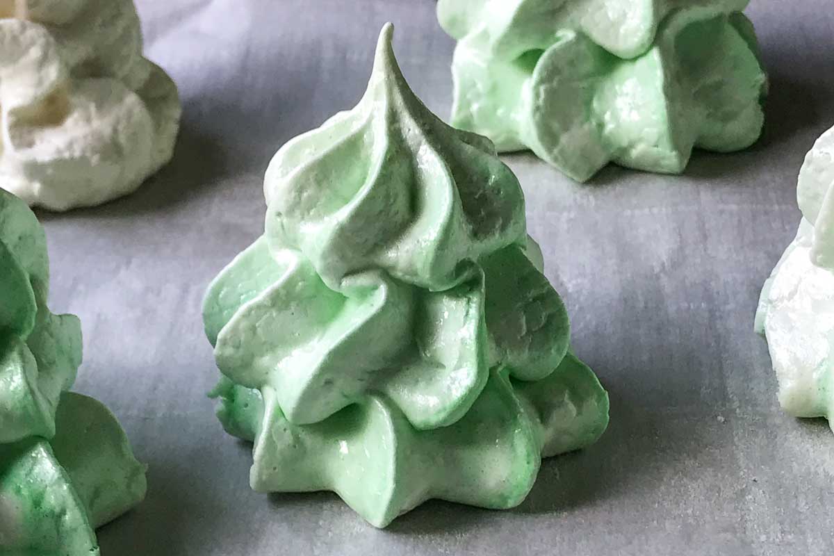 Green and white Christmas tree shaped meringues on parchment paper.