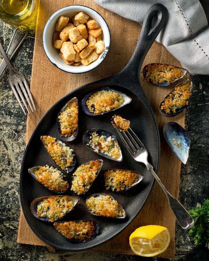 Baked mussels in cast iron pan with lemon and croutons