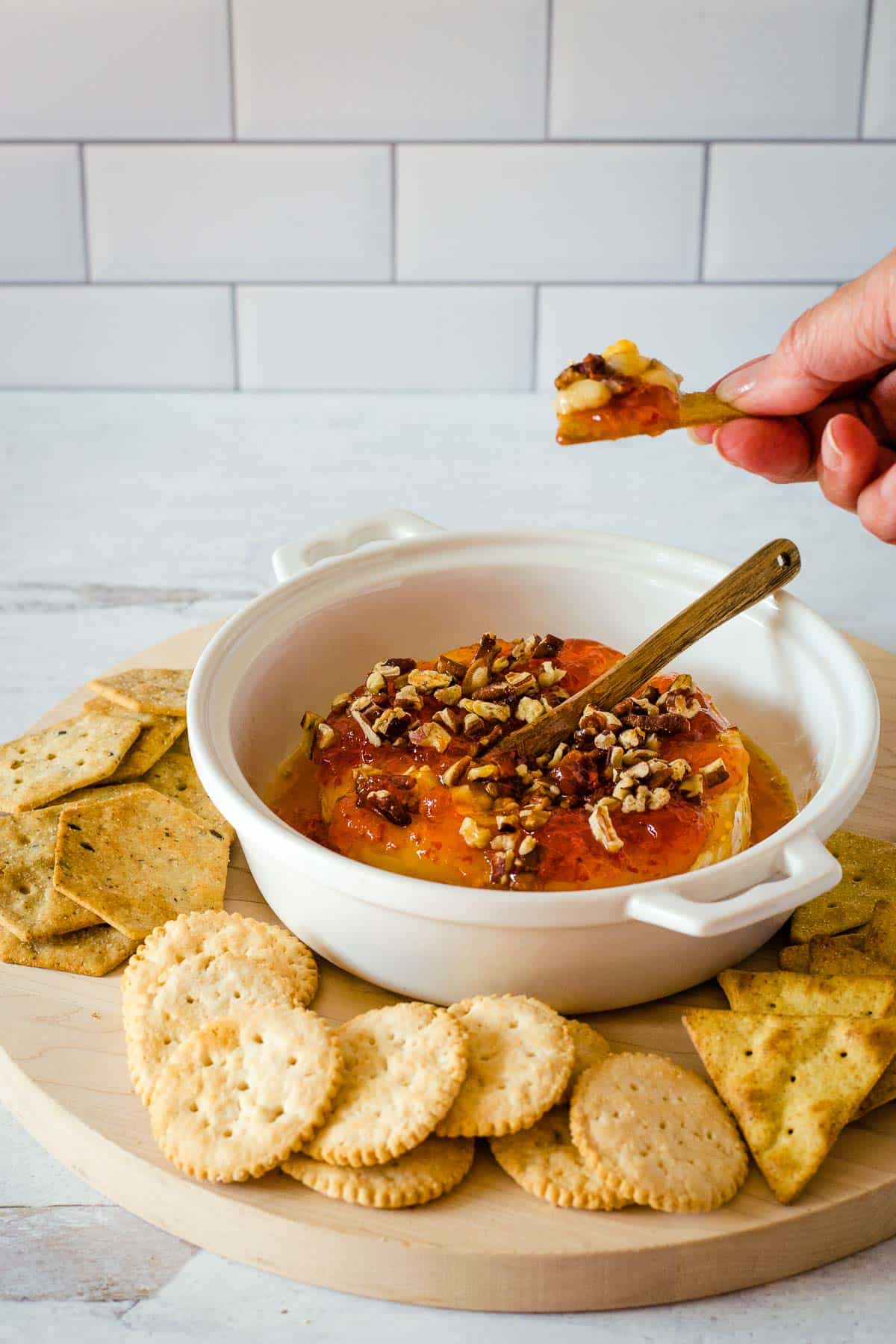 Hand dipping cracker into Baked brie with pepper jelly