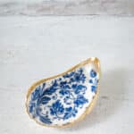 Decoupage oyster shell with blue and white pattern and gold trim.