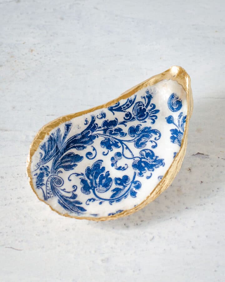 Decoupage oyster shell with blue and white pattern and gold trim.