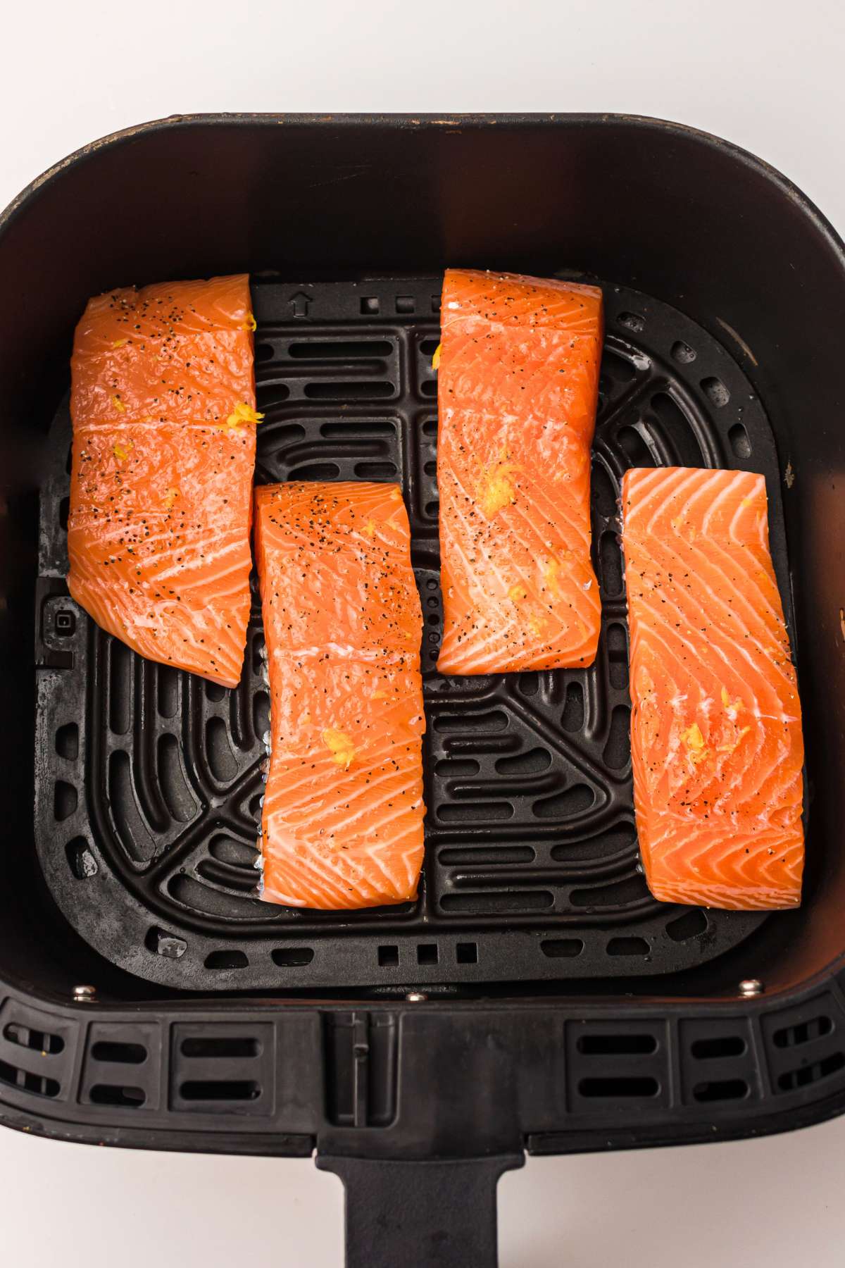 Uncooked salmon in air fryer basket.