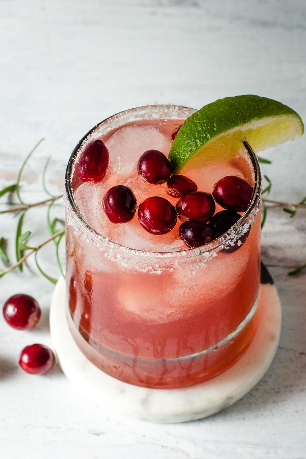 Cranberry margarita with fresh cranberries, rosemary and lime wedge.