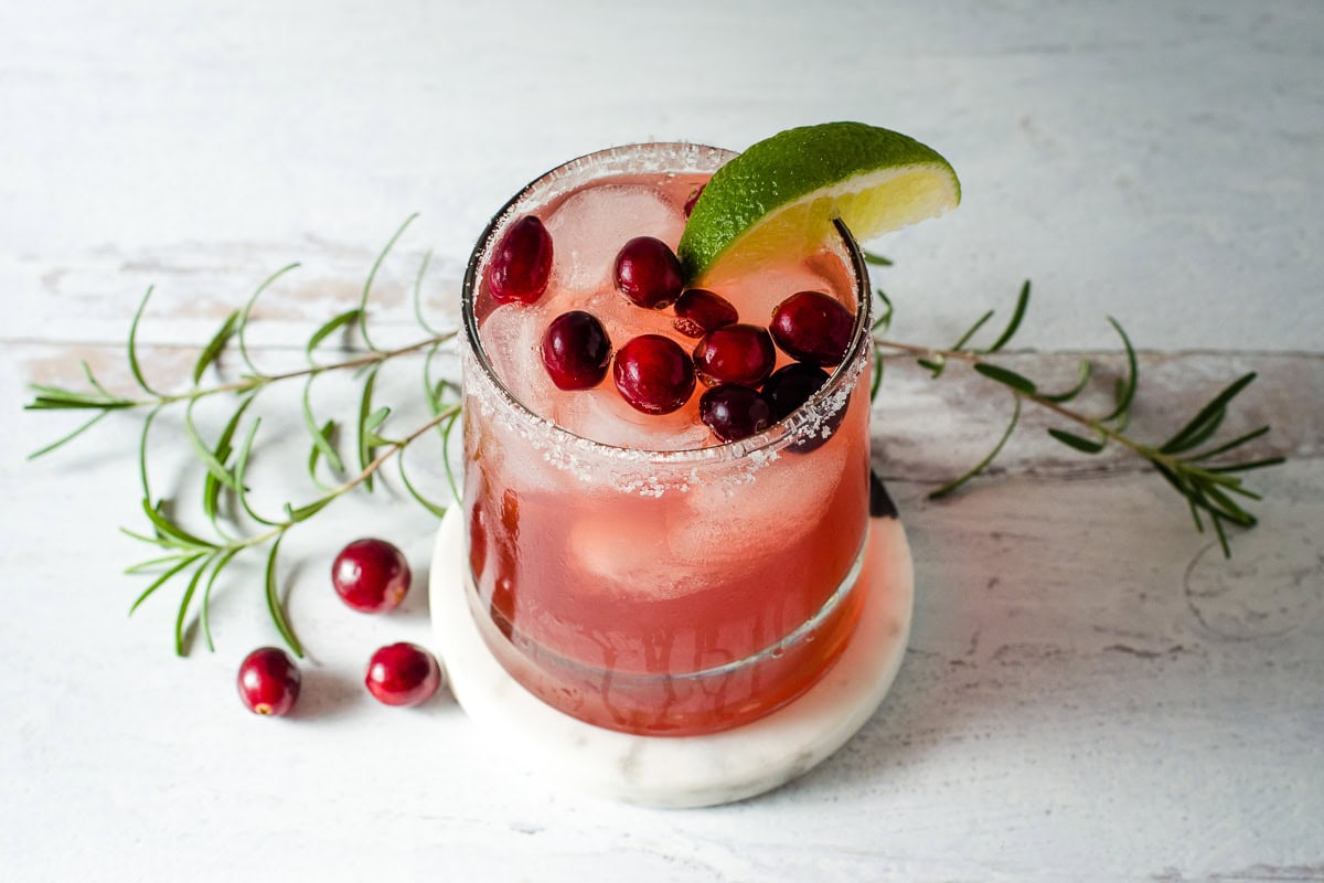 Cranberry margarita with fresh cranberries, rosemary and lime wedge.