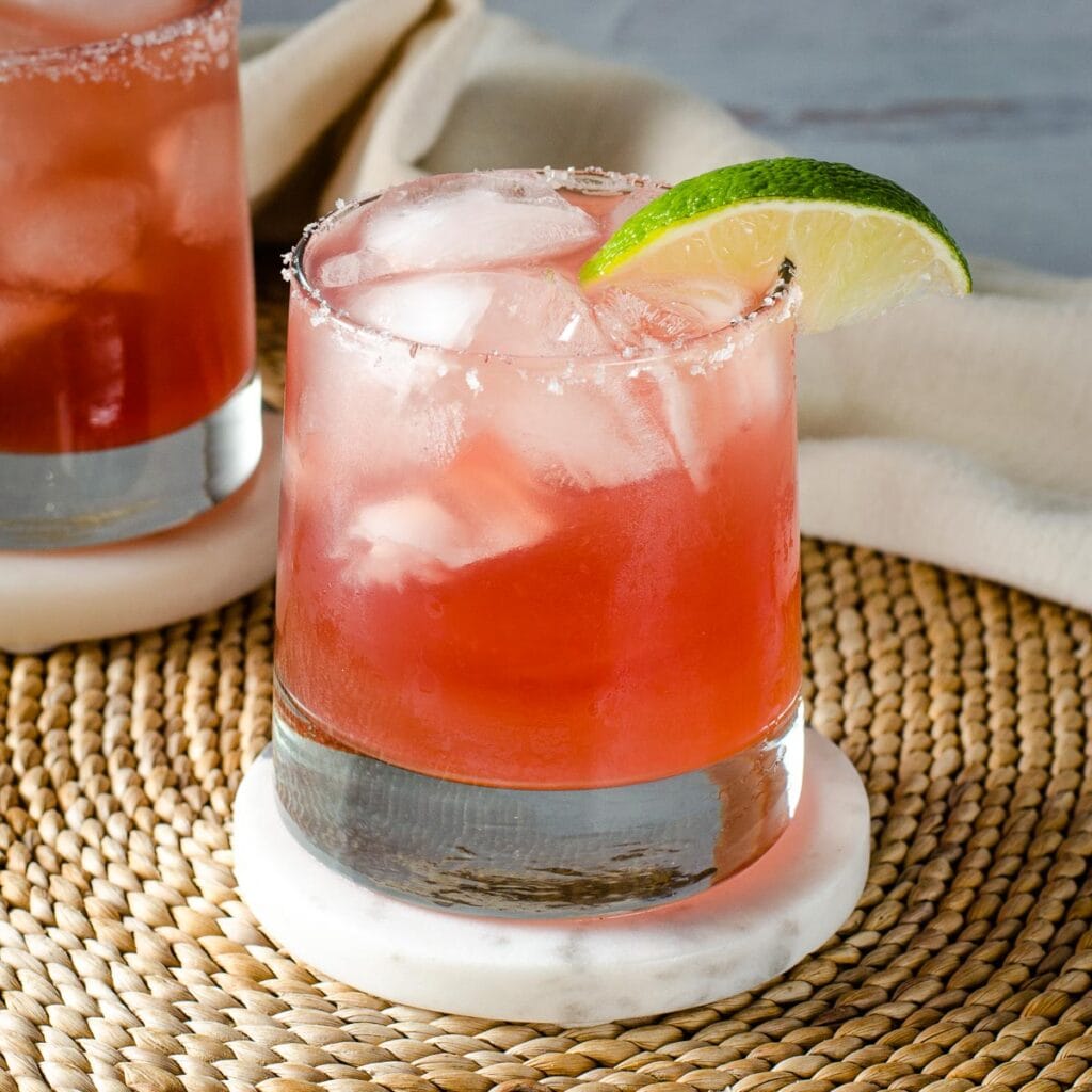 Cranberry margarita with salted rim and lime wedge.