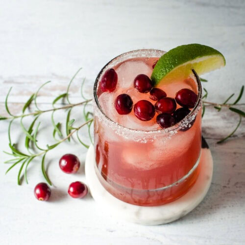 Cranberry margarita with fresh cranberries, rosemary and lime wedge.
