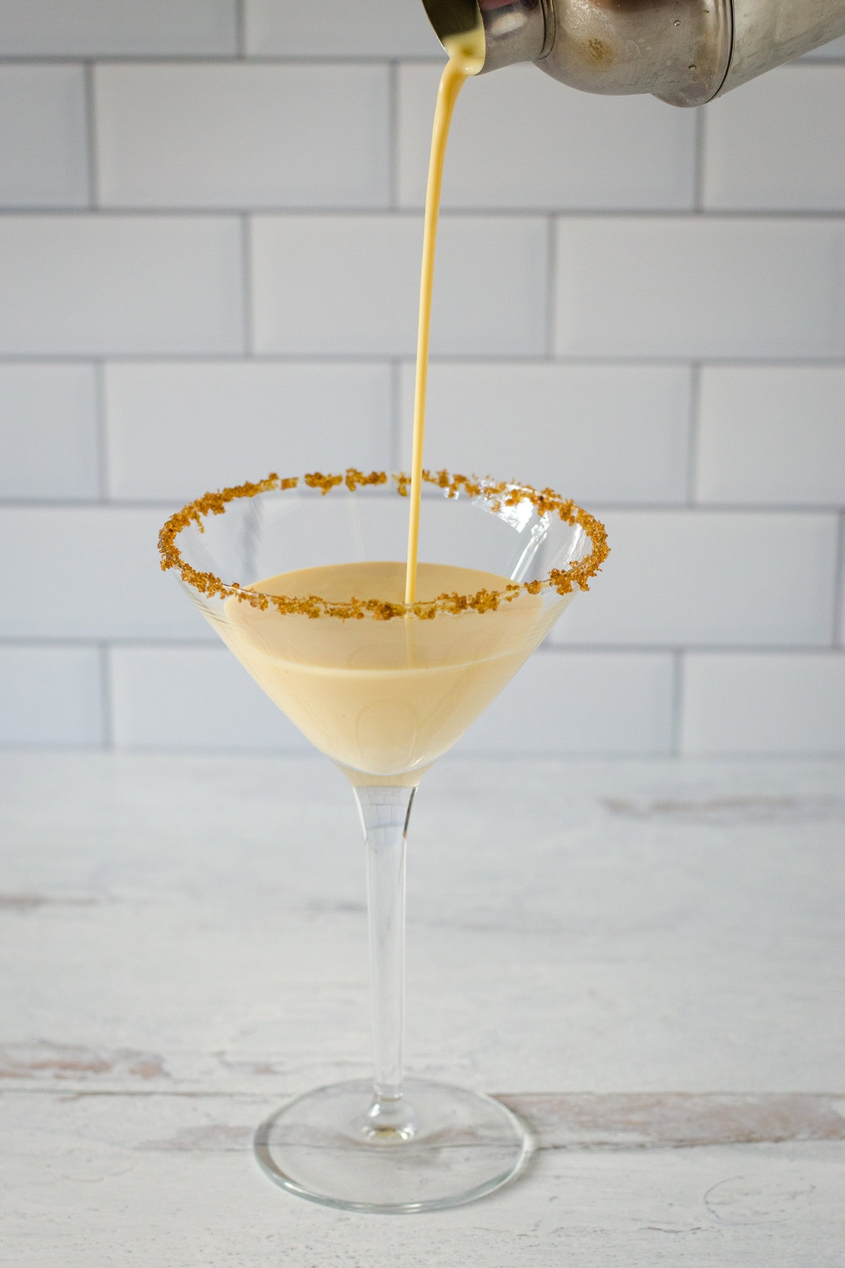 Drink shaker pouring eggnog martini into sugar rimmed cocktail glass.