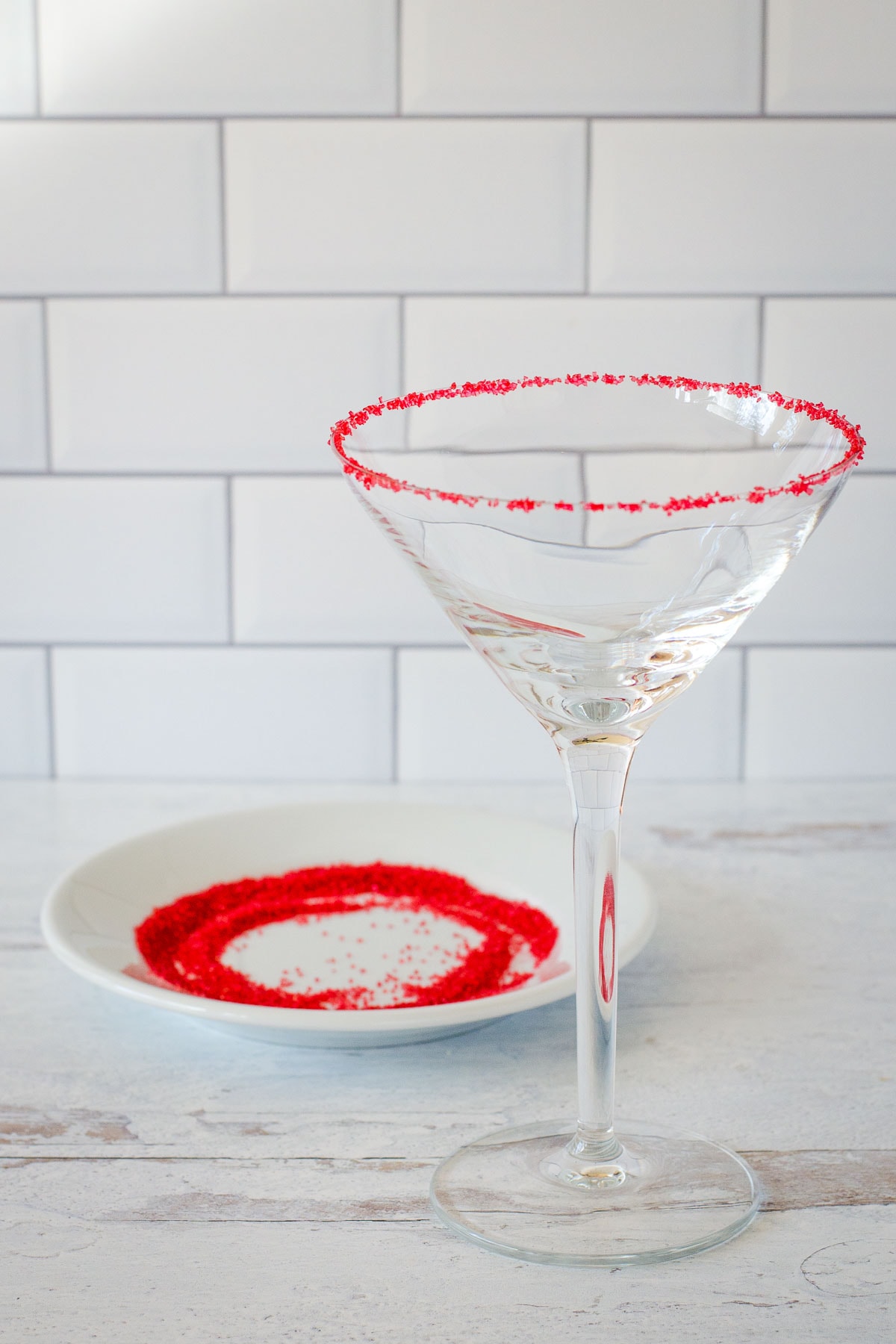 Cocktail glass rimmed with red sugar with small plate of red sugar.