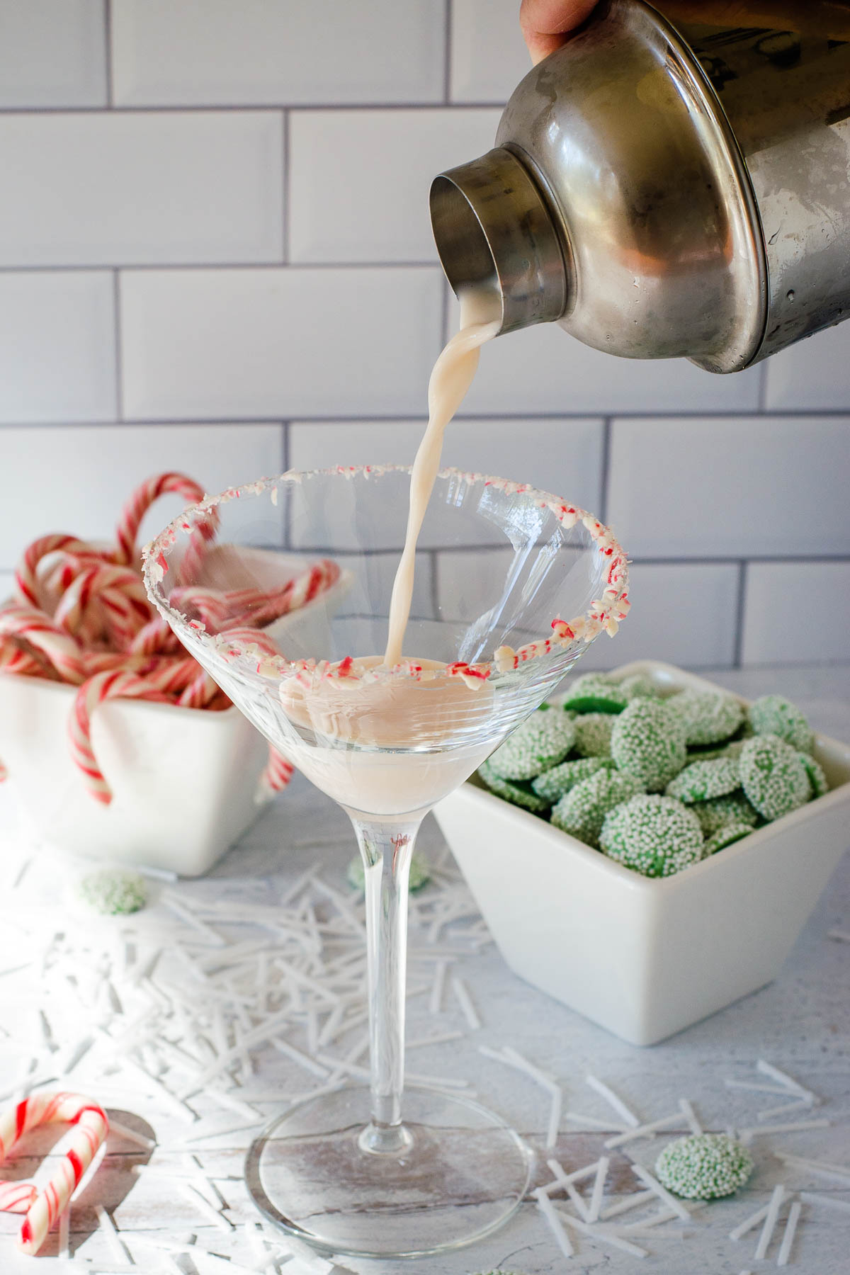 Cocktail shaker pouring drink into glass with candy in background.