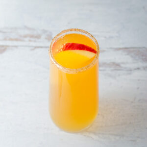 Apple cider mimosa in stemless champagne flute rimmed with cinnamon sugar and garnished with a red apple slice.