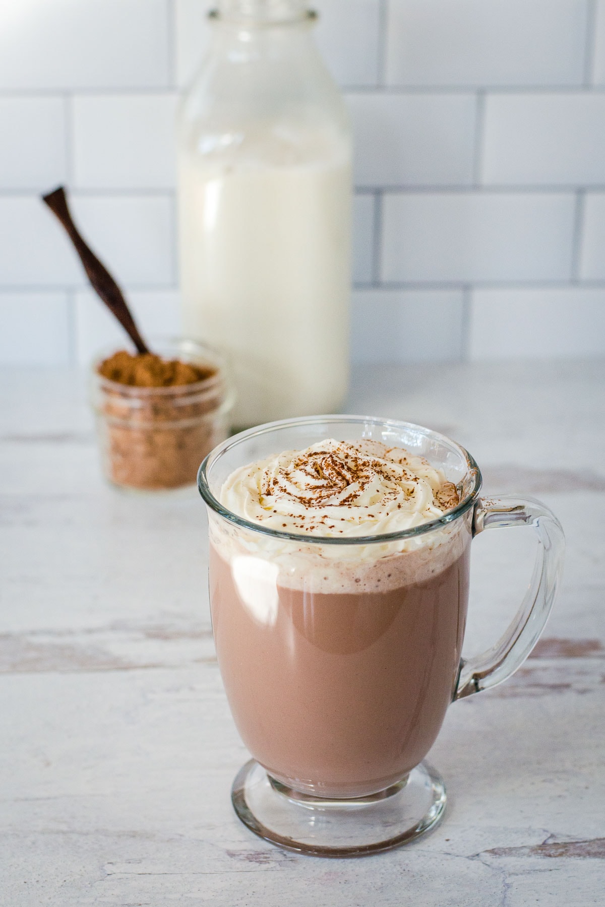 Glass mug with hot chocolate, whipped cream and cocoa.