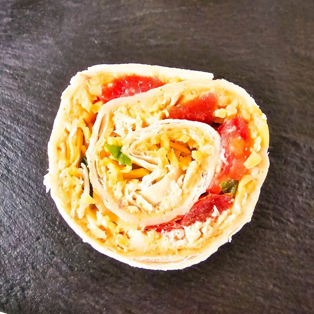 Chicken taco pinwheel filled with chopped vegetables and cheese is on a black serving tray.