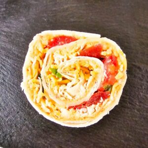 Chicken taco pinwheel filled with chopped vegetables and cheese is on a black serving tray.