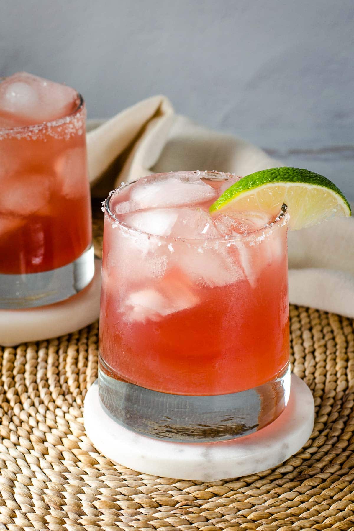 Cranberry margaritas with lime wedge on coasters.