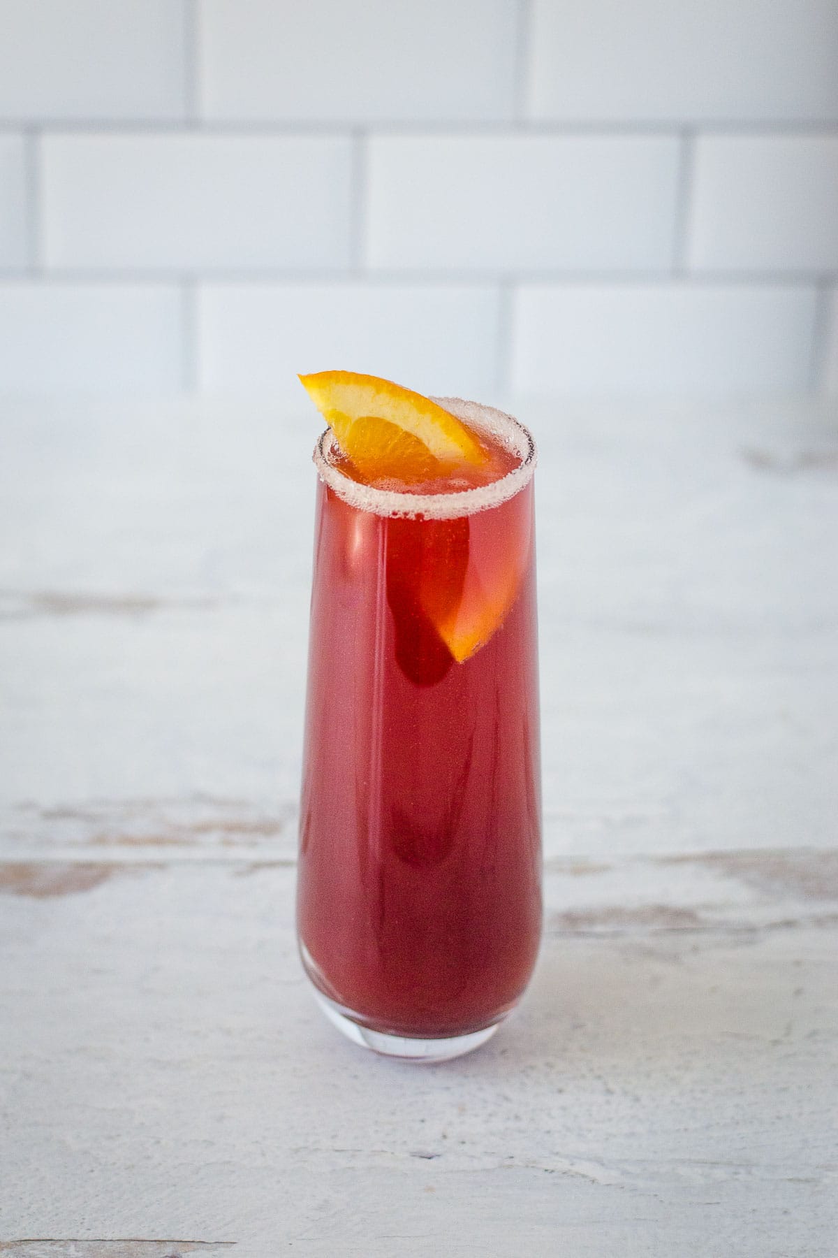 Cranberry mimosa in stemless flute with orange slice garnish.