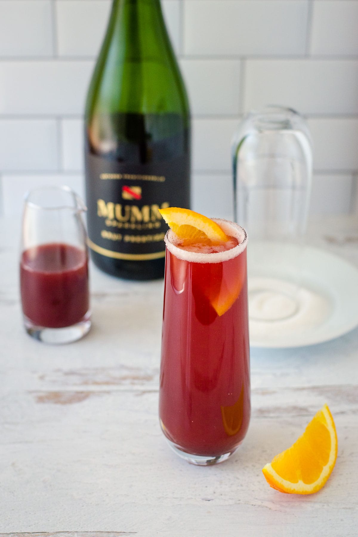 Cranberry mimosa with cranberry juice, champagne, glass dipped in sugar and orange slices.