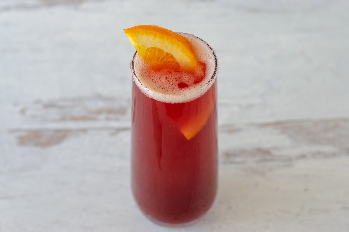 Sparkling red drink in stemless flute with orange slice garnish.