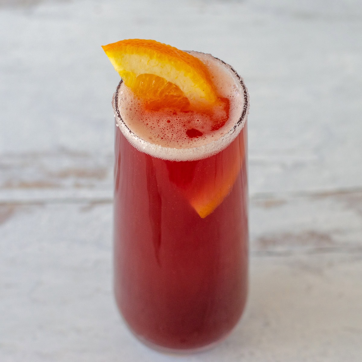 Cranberry mimosa in stemless flute with orange slice garnish.