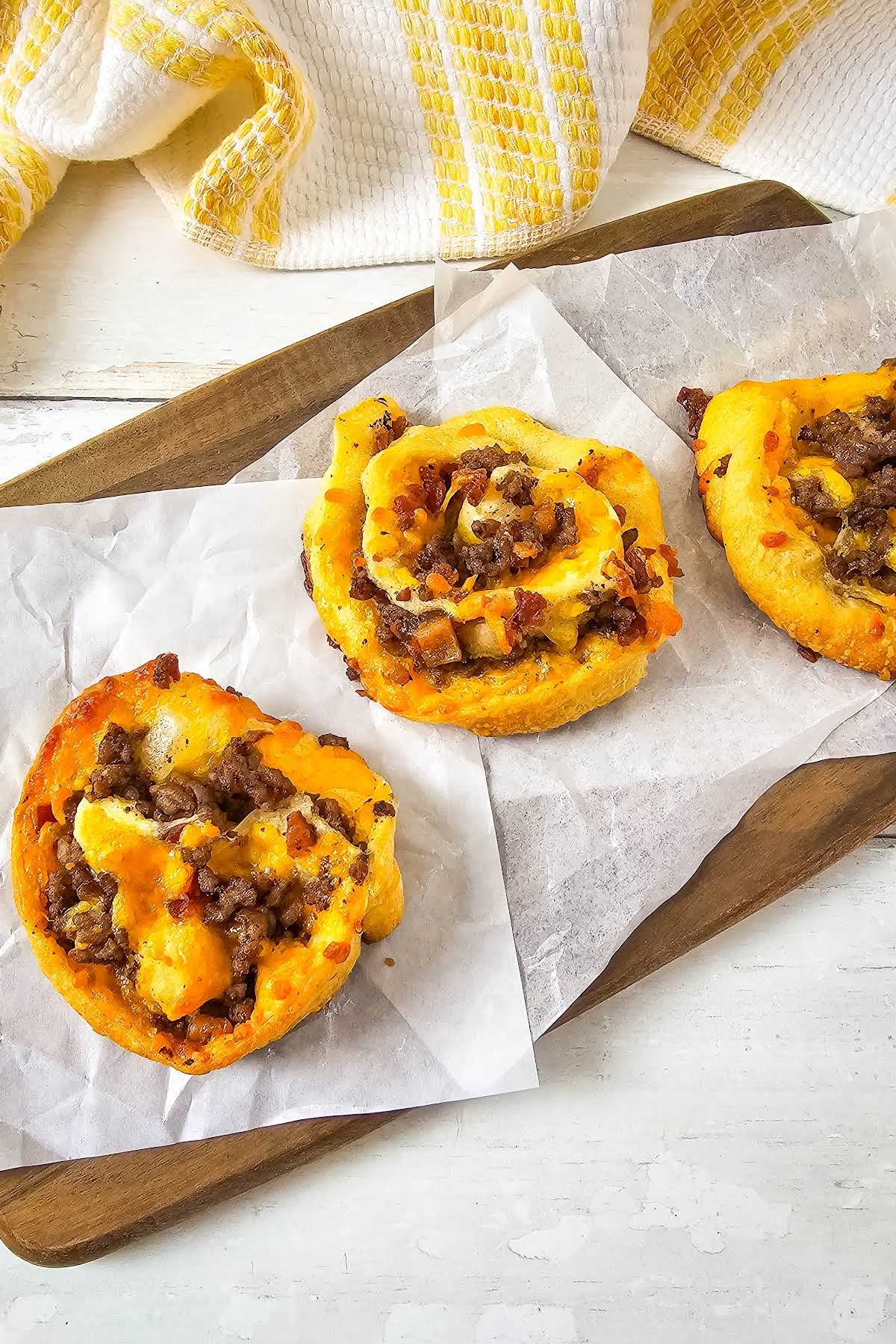 Bacon cheeseburger pinwheels on parchment lined cutting board.