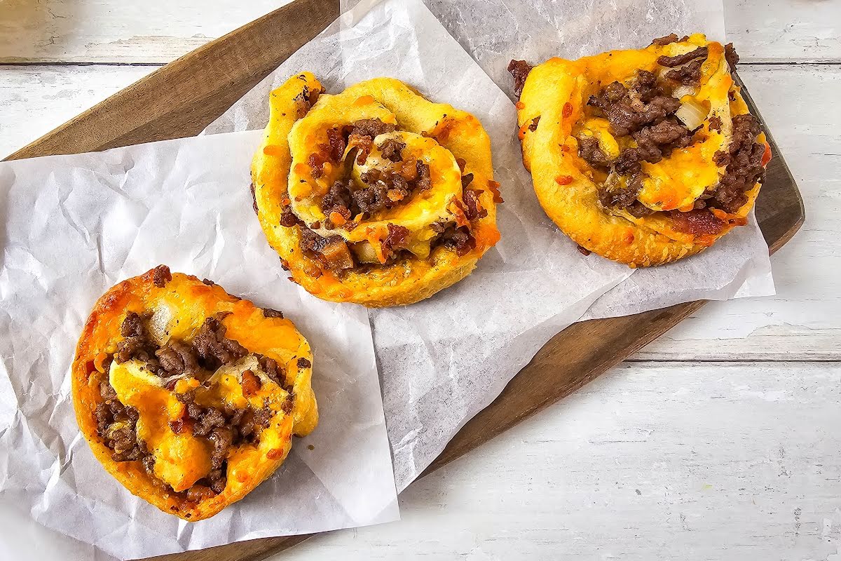 Bacon cheeseburger pinwheels on parchment lined cutting board.