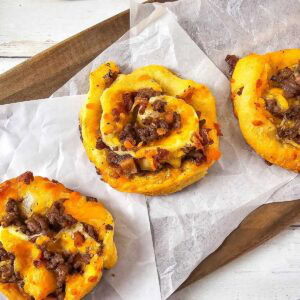 Bacon cheeseburger pinwheels on parchment lined cutting board.