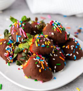 Chocolate covered strawberries with sprinkles on white plate.