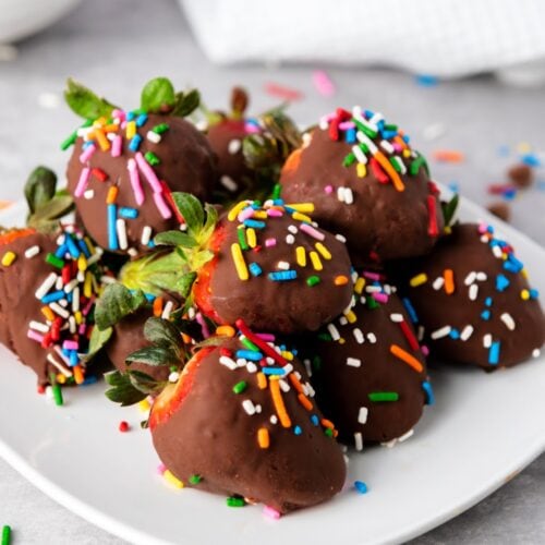 Chocolate covered strawberries with sprinkles on white plate.