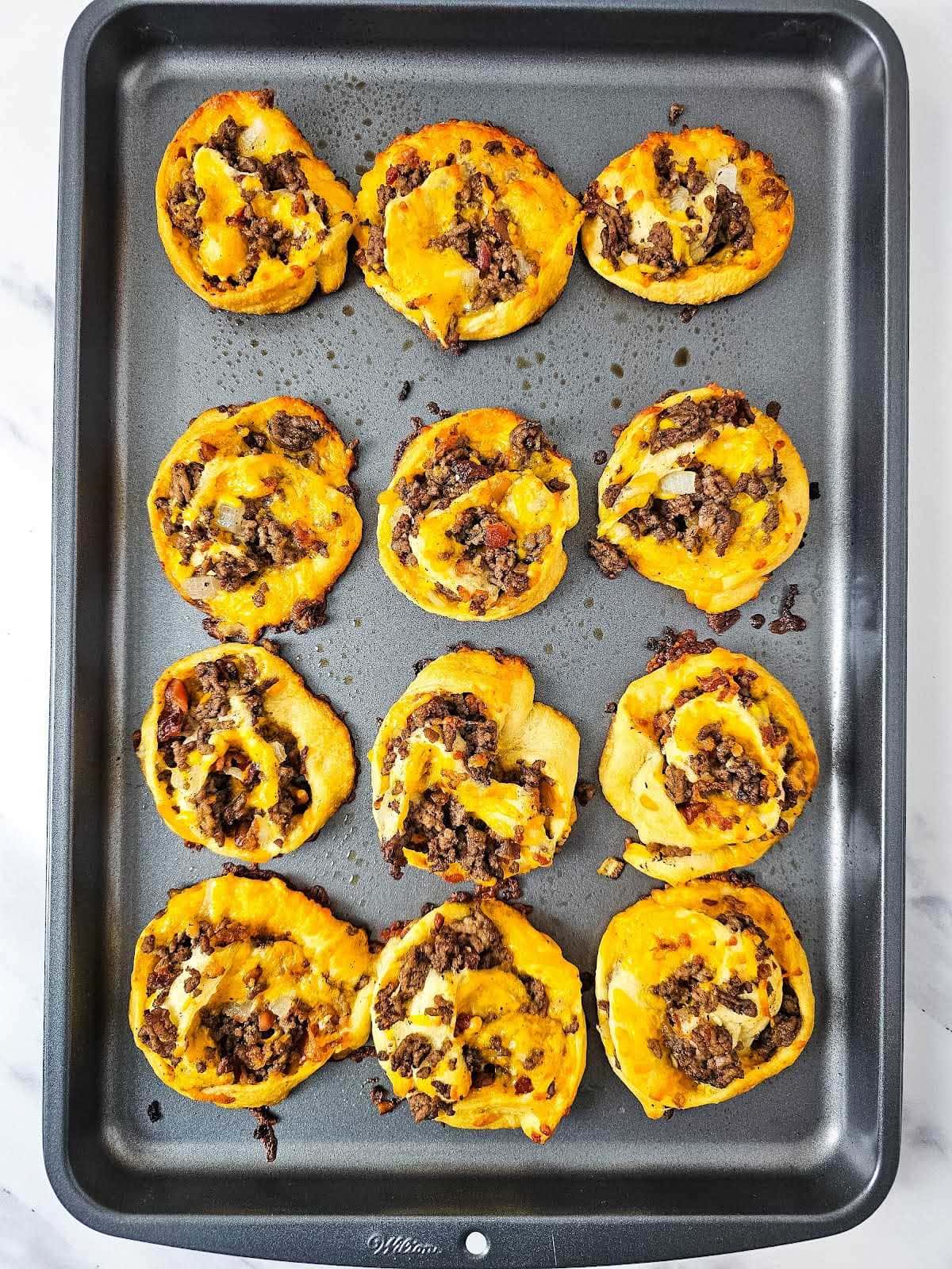 Bacon cheeseburger pinwheels on baking sheet.