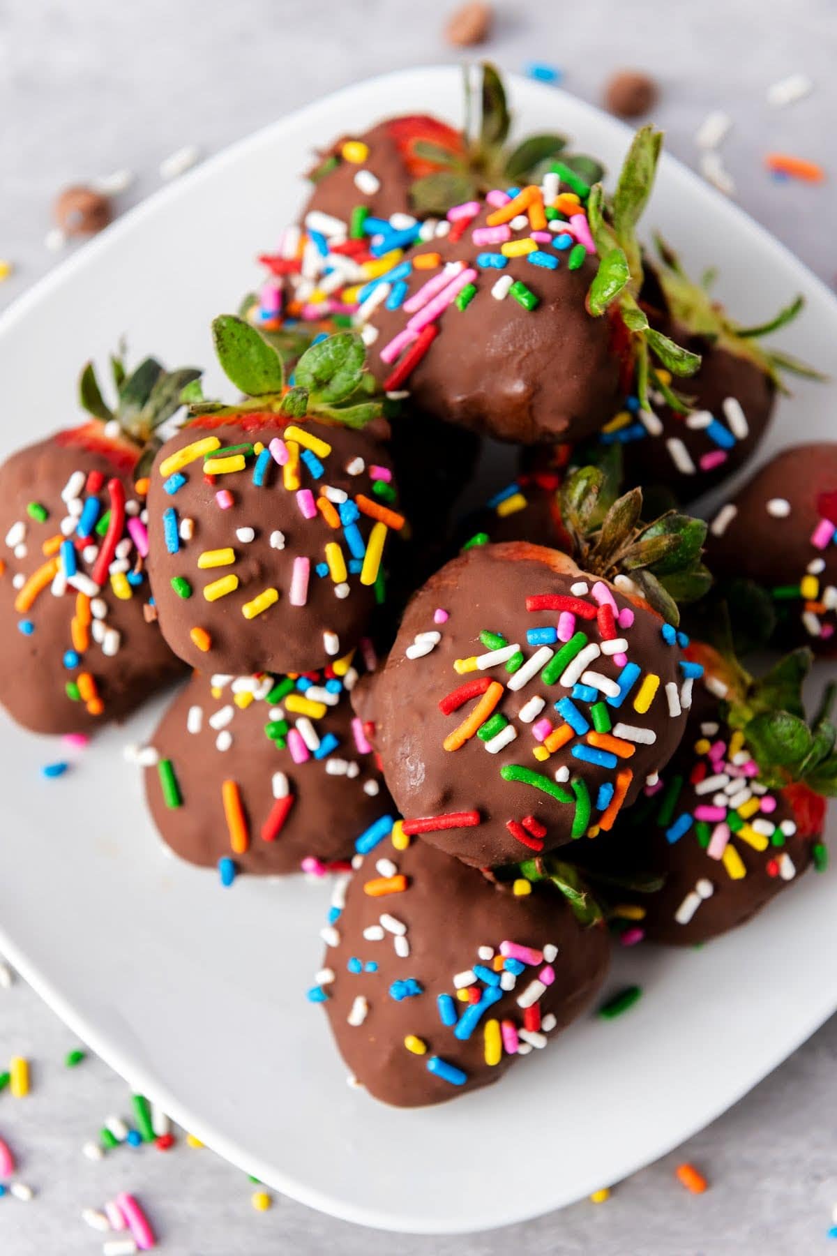 Chocolate covered strawberries with rainbow sprinkles on white plate.