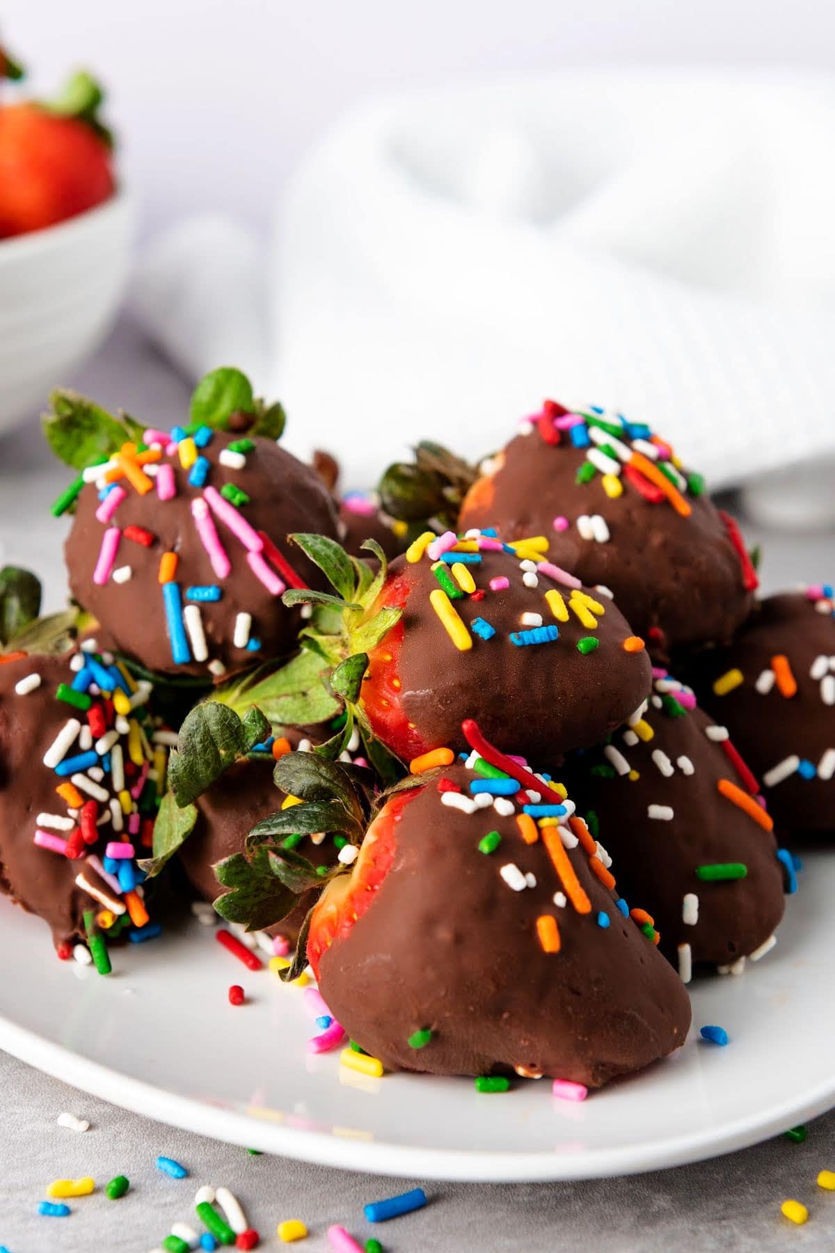 Chocolate covered strawberries with sprinkles on white plate.