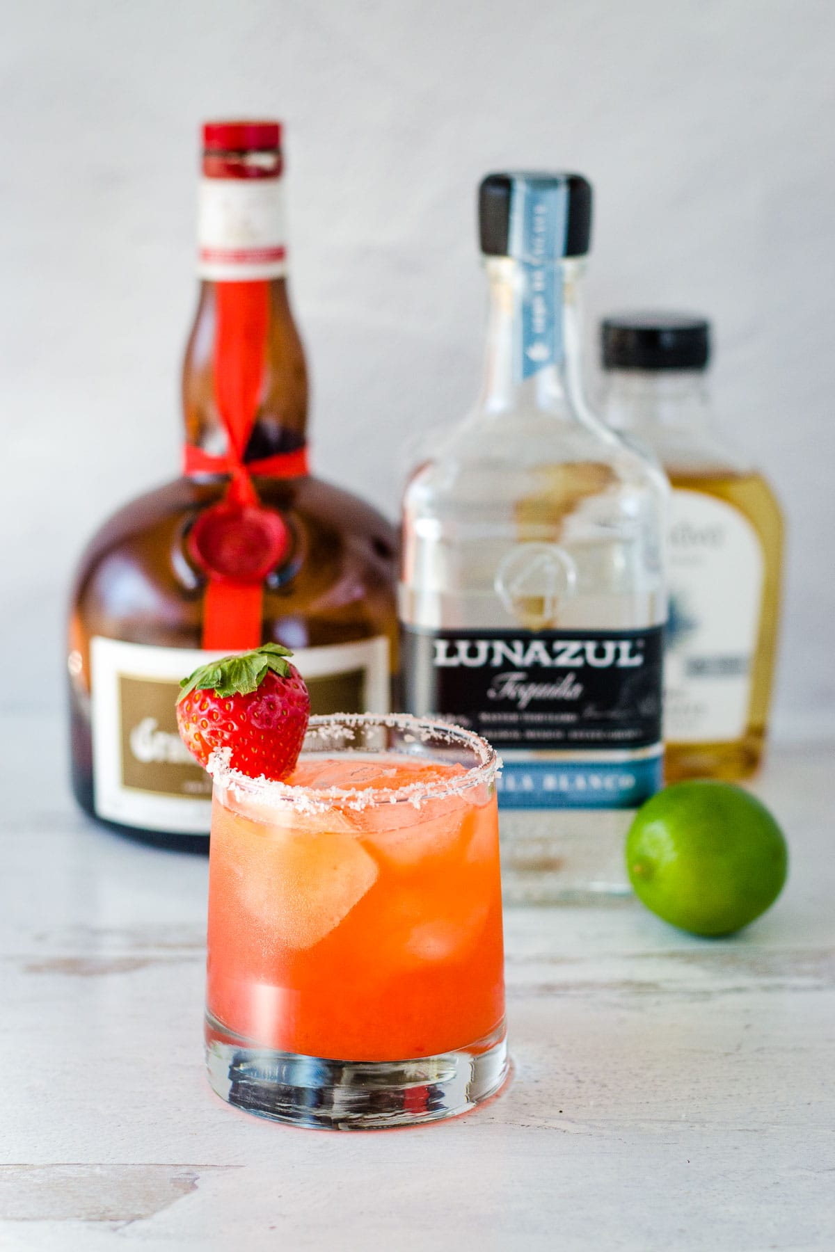 Strawberry margarita with orange liqueur, tequila, agave and lime in background.