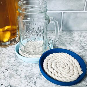 Nautical blue painted clay coasters with rope on counter with glass mason jar mug.