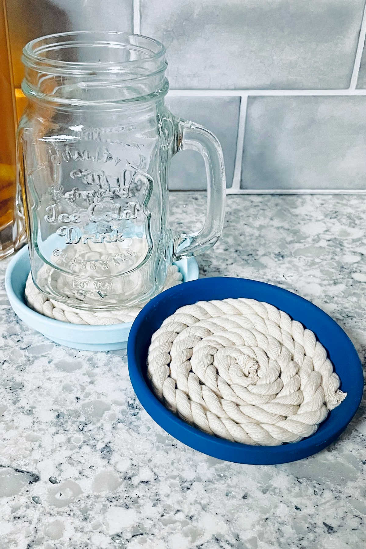 Dark blue clay and rope coaster with light blue coaster and glass in background.