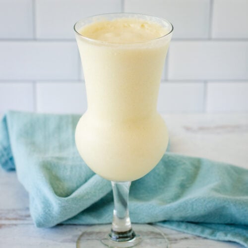 Frozen pina colada in tall glass with blue towel in background.