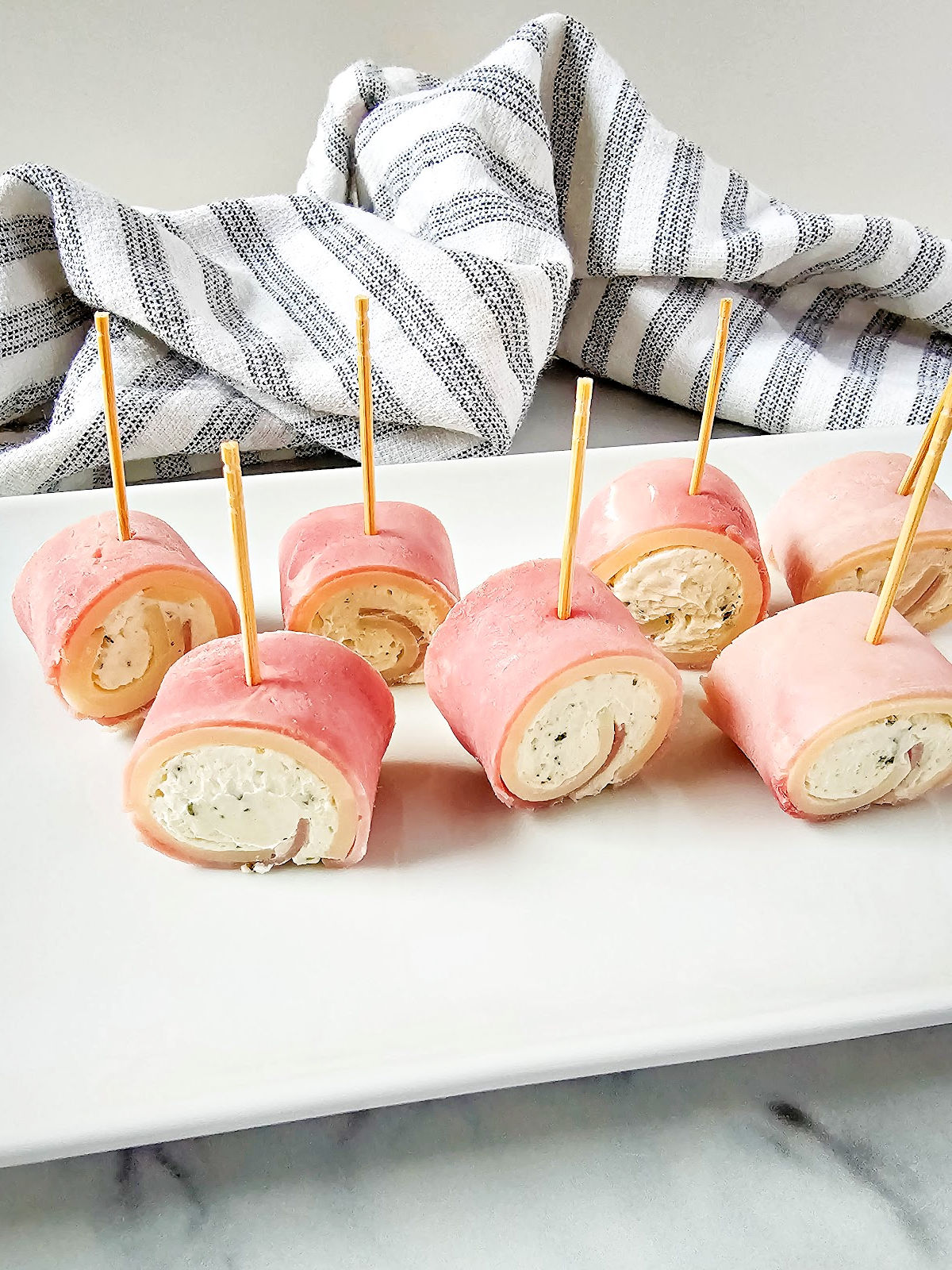 Ham roll ups with cream cheese arranged on serving plate.