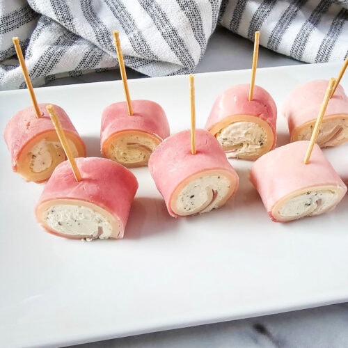 Ham cream cheese roll ups with toothpicks on plate.